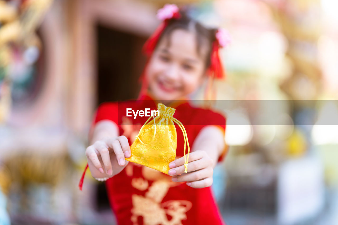 Portrait of smiling girl holding golden bag while sanding outdoors