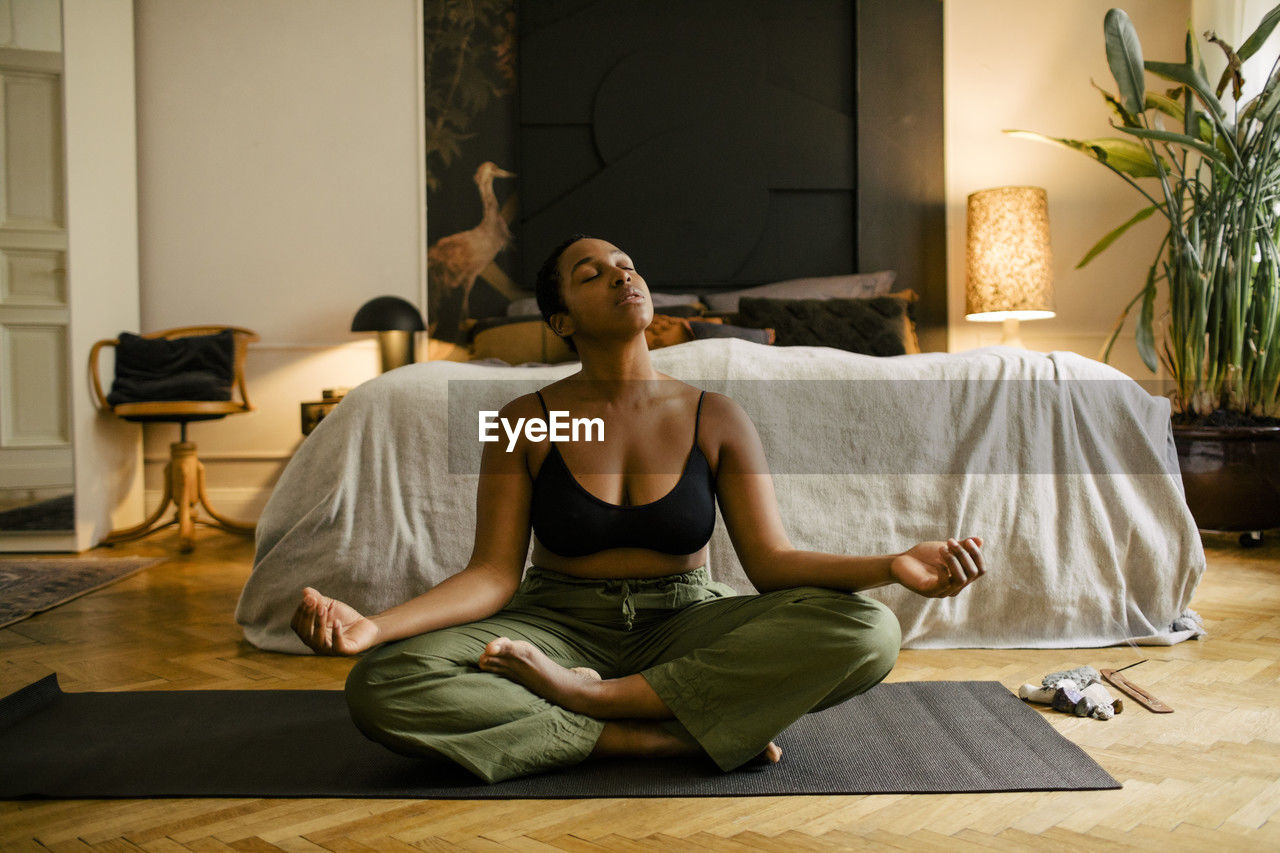 Young woman meditating on exercise mat in bedroom at home