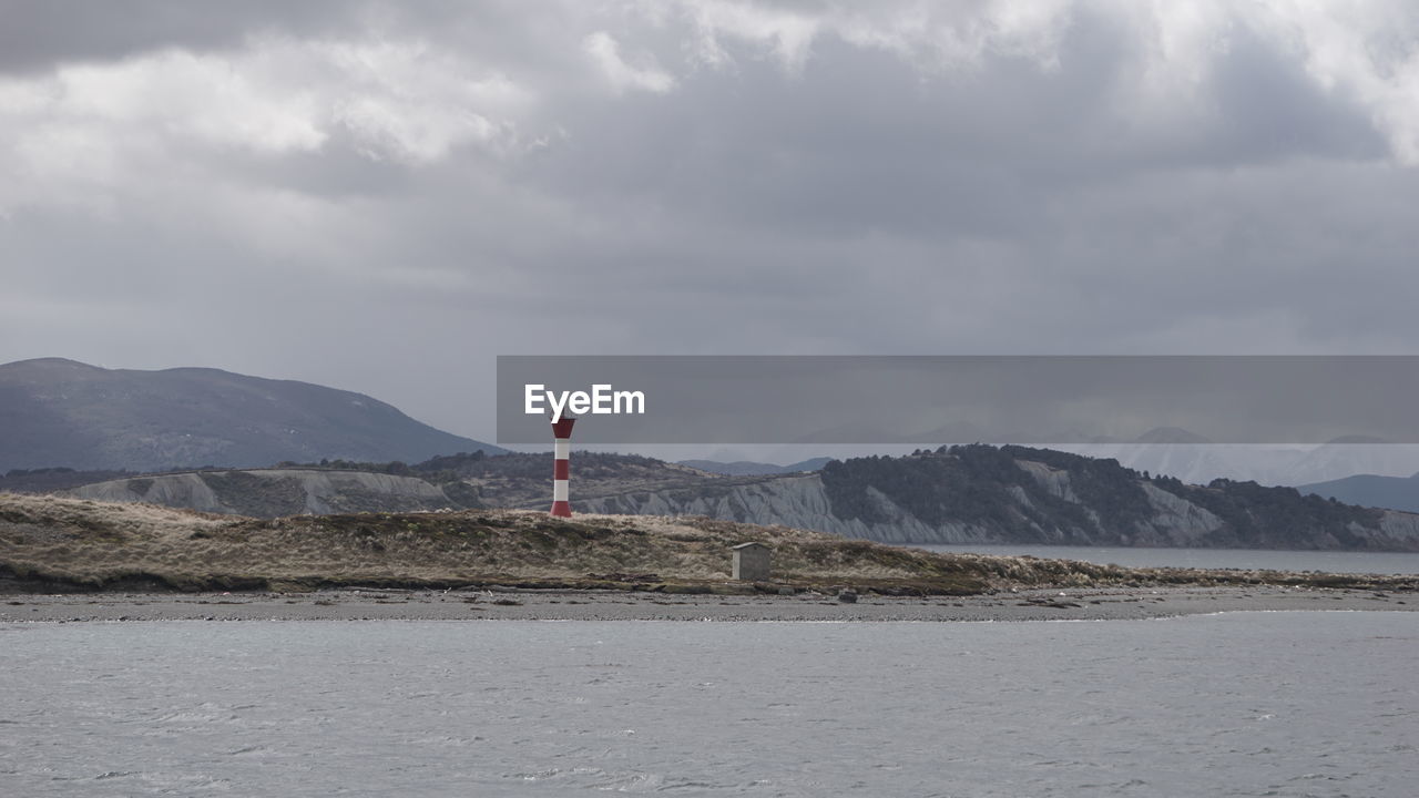 Lighthouse amidst buildings and mountains against sky