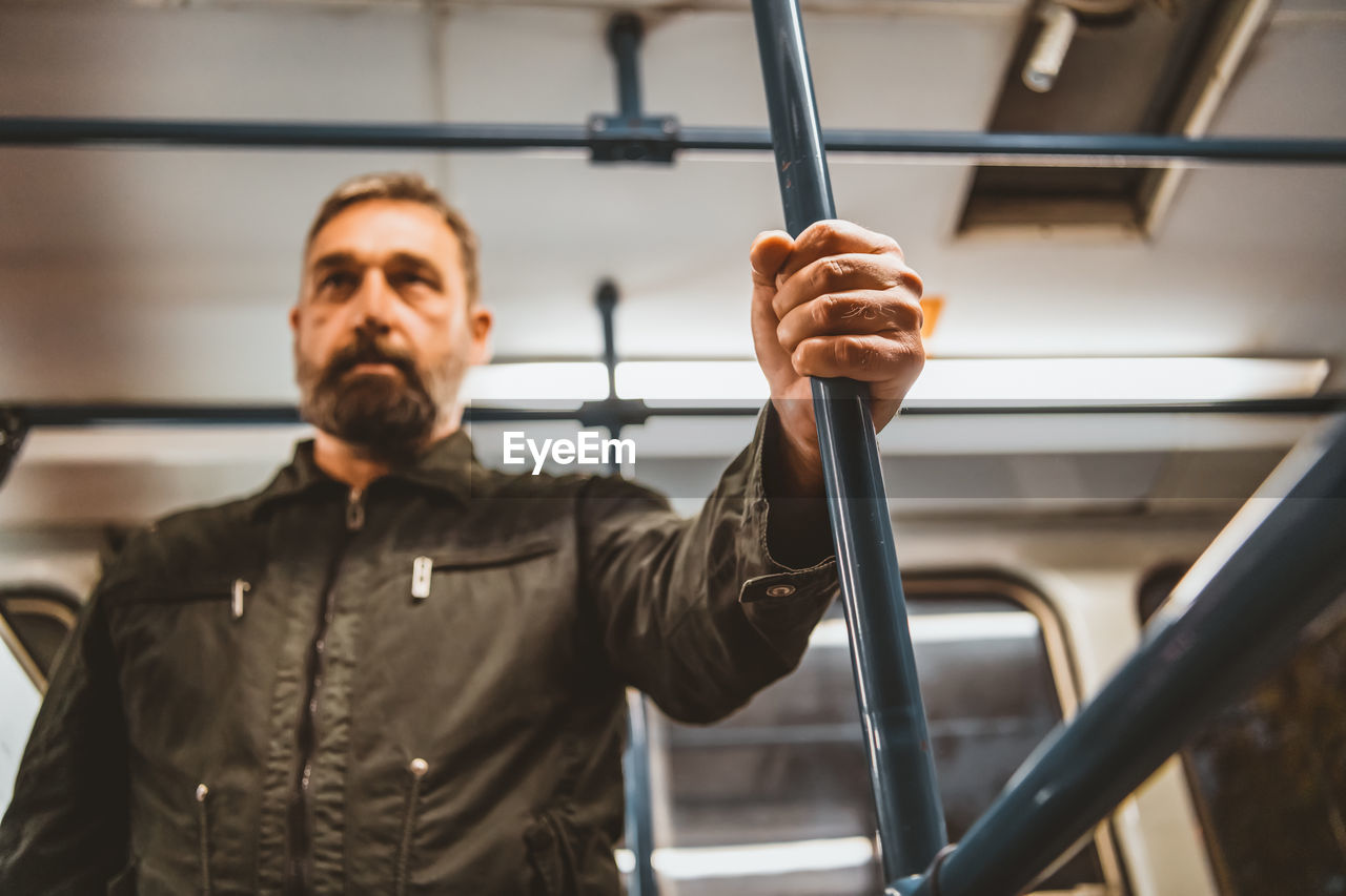 Middle-aged caucasian man driving in the city bus while standing and holding grip.