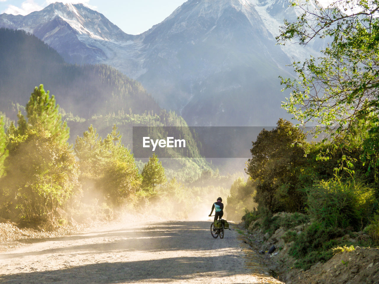 Man riding bicycle on dirt road against mountains