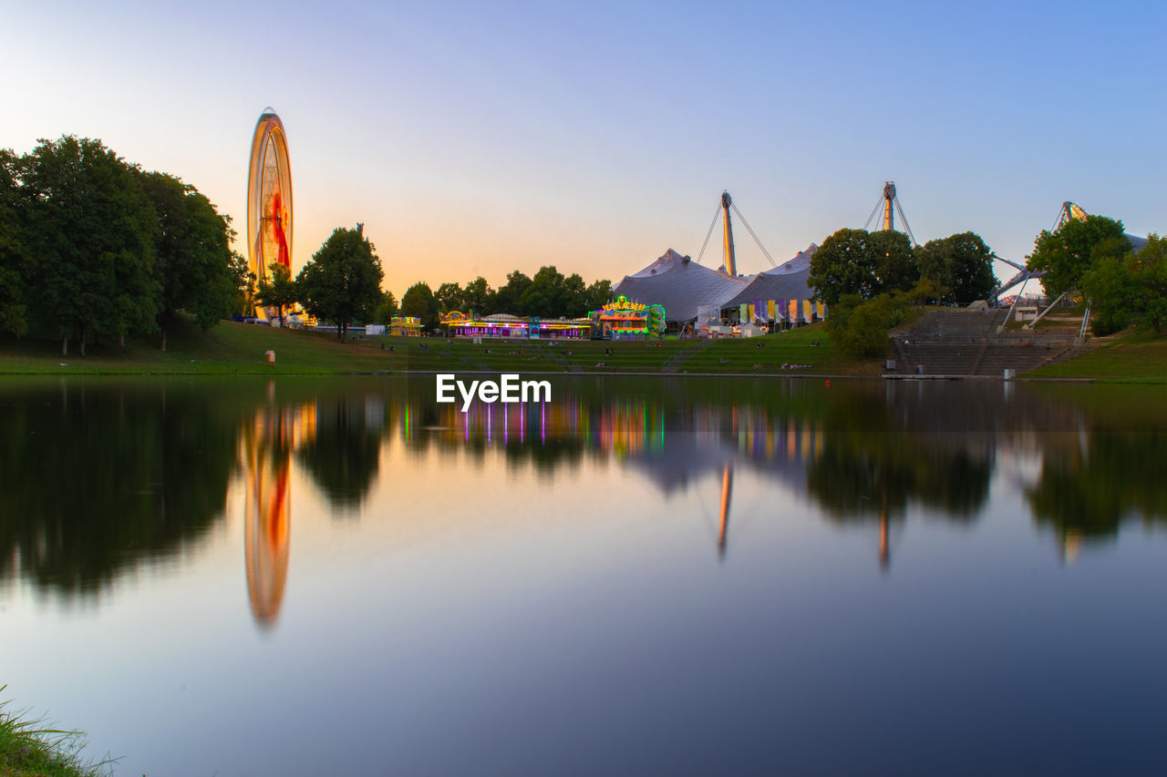 Reflection of trees, lights and ferris wheel in lake 