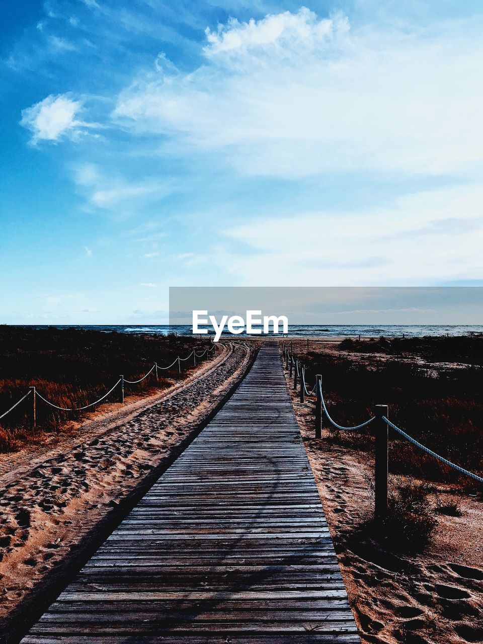 Boardwalk leading towards sea against sky