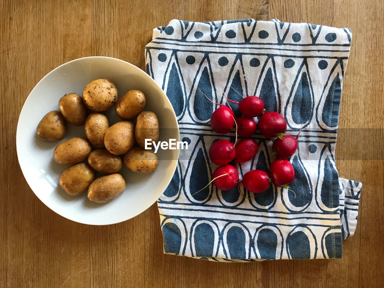 High angle view of potatoes and radishes in plate on a tablecloth on a wooden table