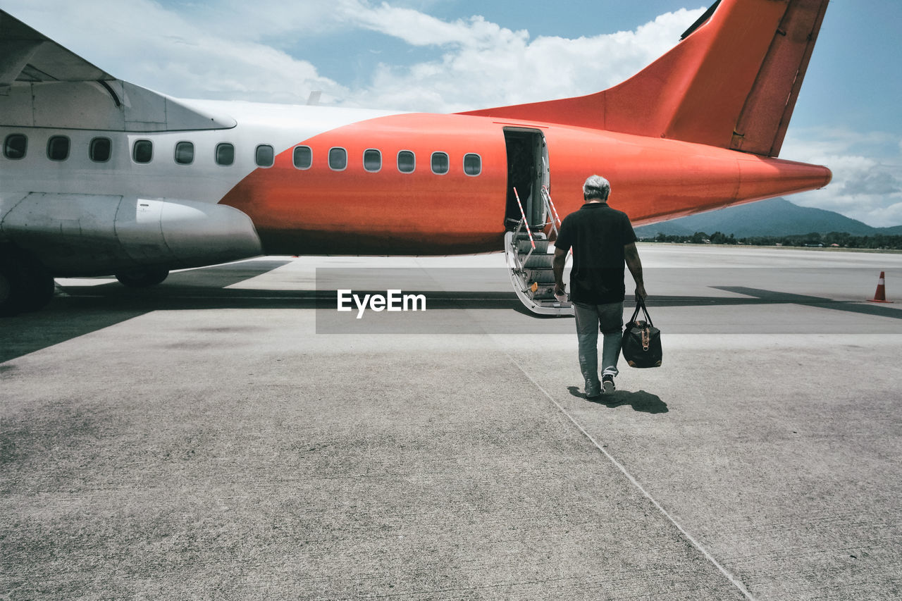 Rear view of man on airport runway against sky