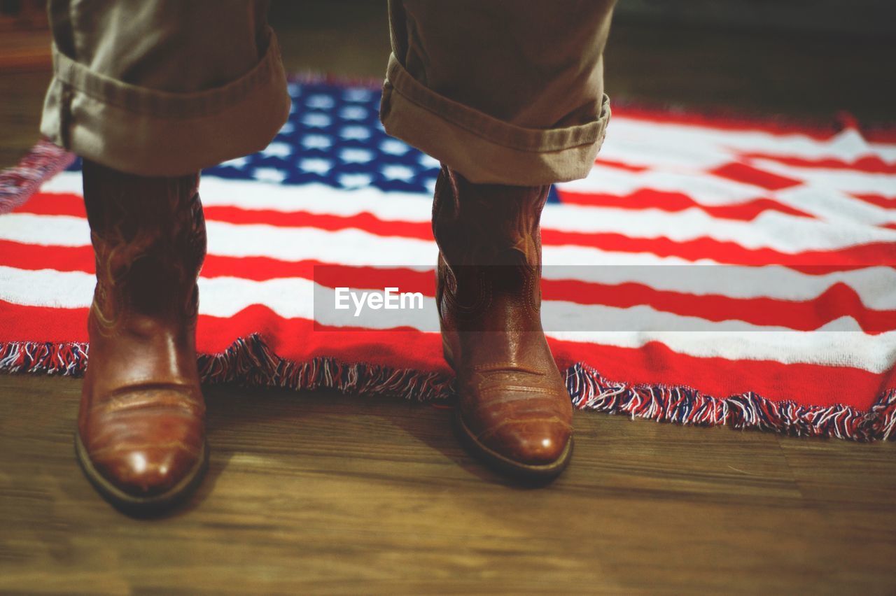 Low section of person by american flag on hardwood floor