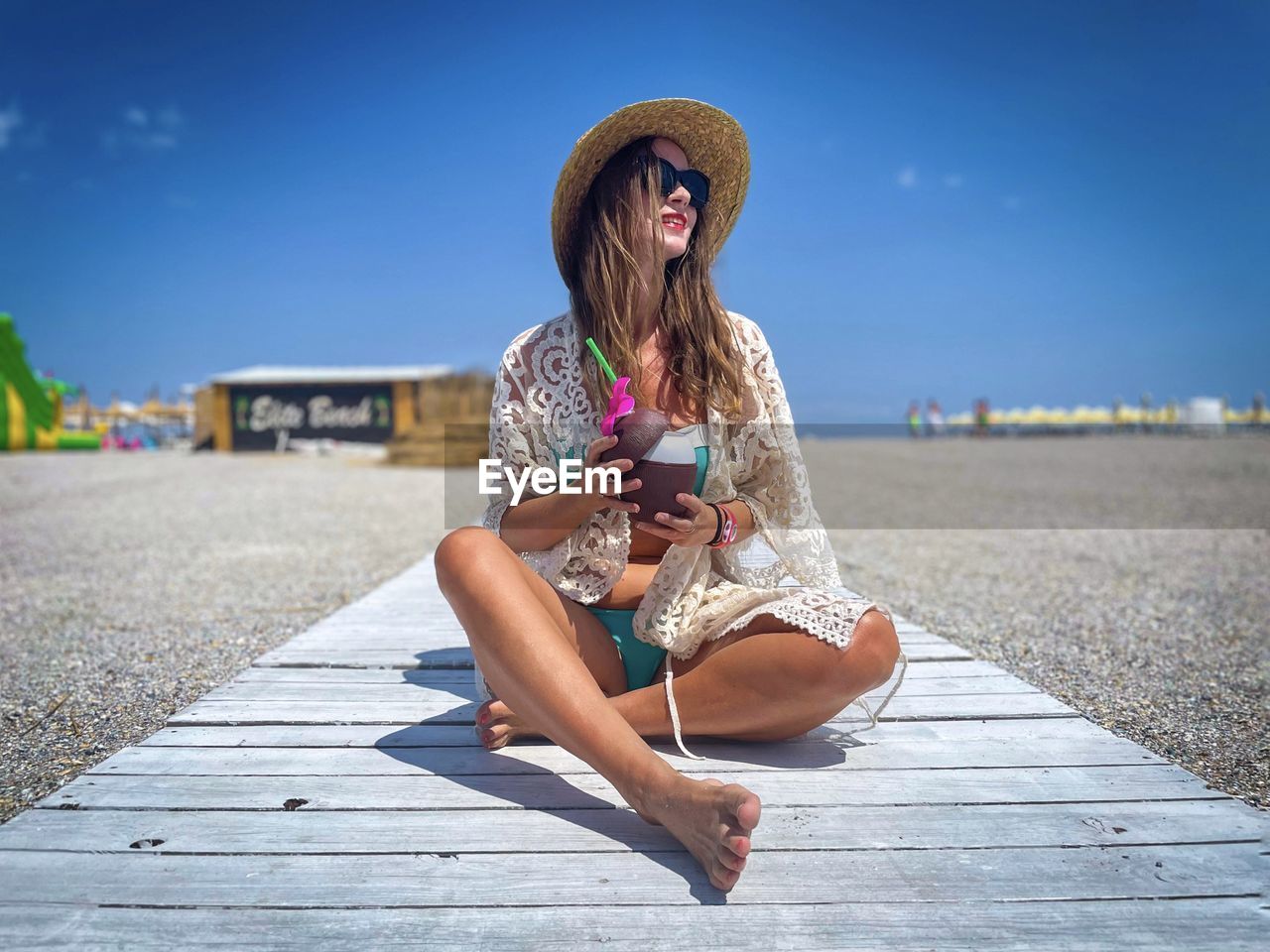 Fashionable young woman on the beach holding a cocktail in her hand