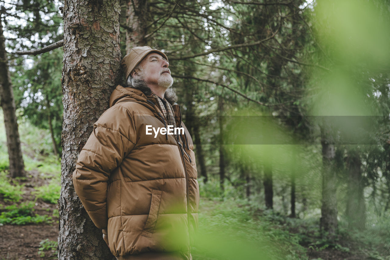 Senior man wearing jacket standing by tree in forest