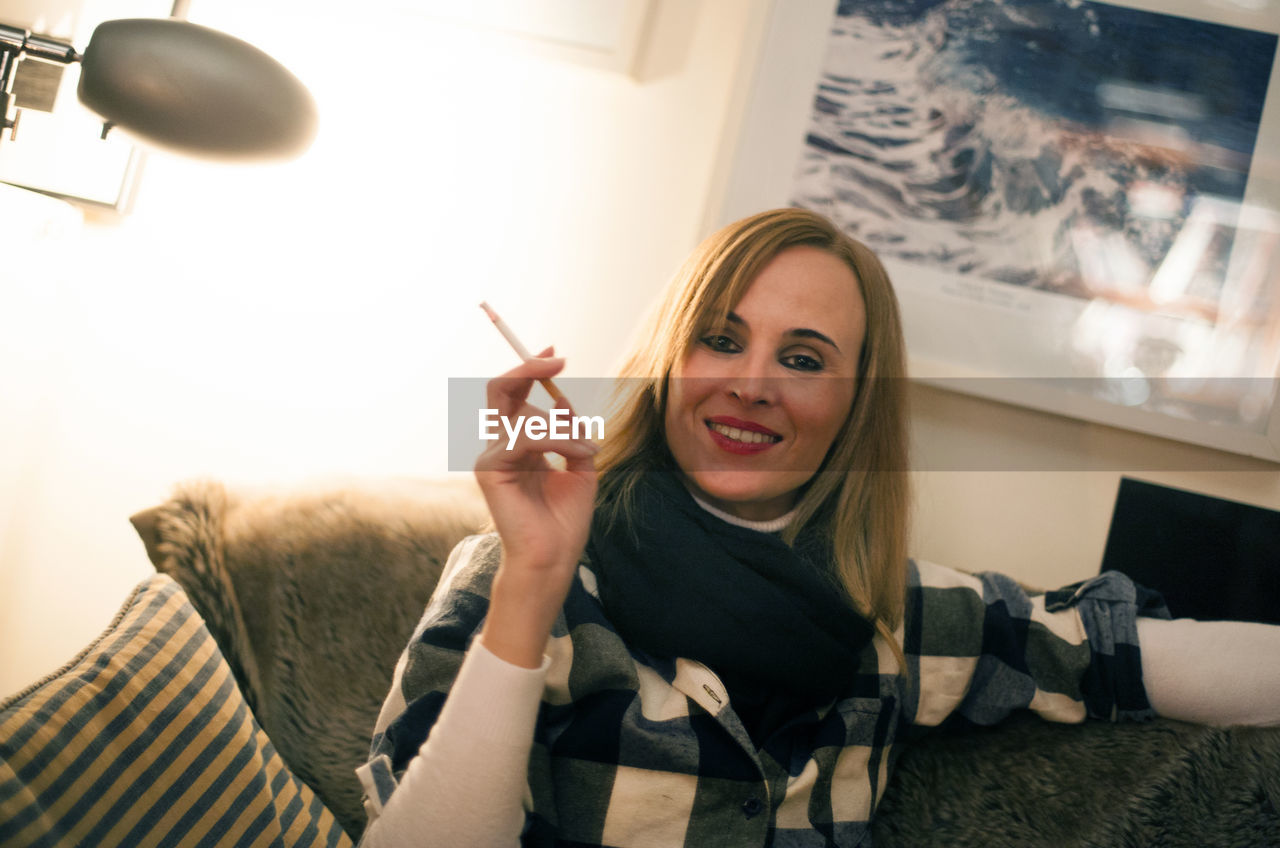 Portrait of beautiful woman holding cigarette while sitting on sofa