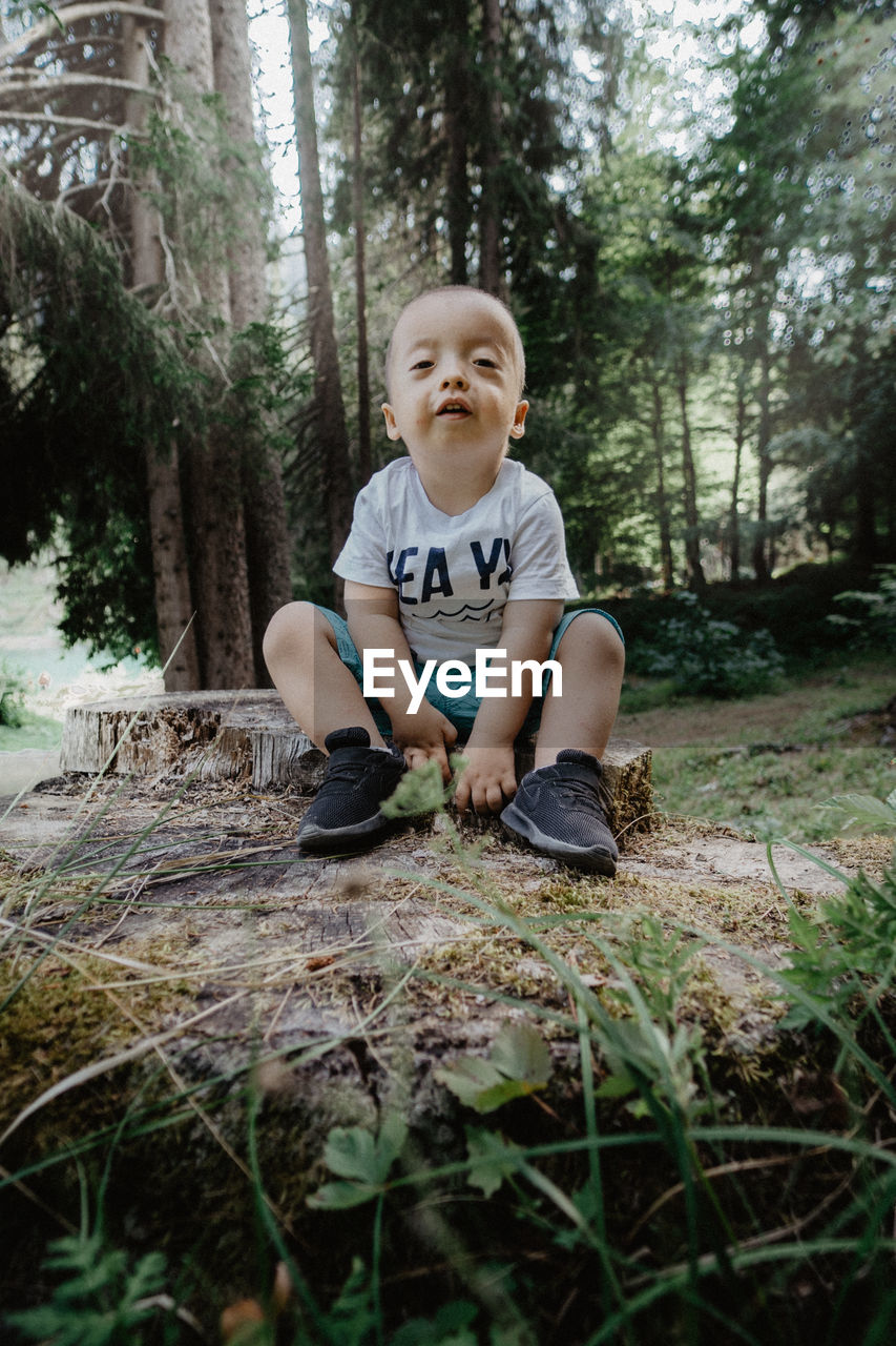 FULL LENGTH PORTRAIT OF BOY SITTING IN A FOREST