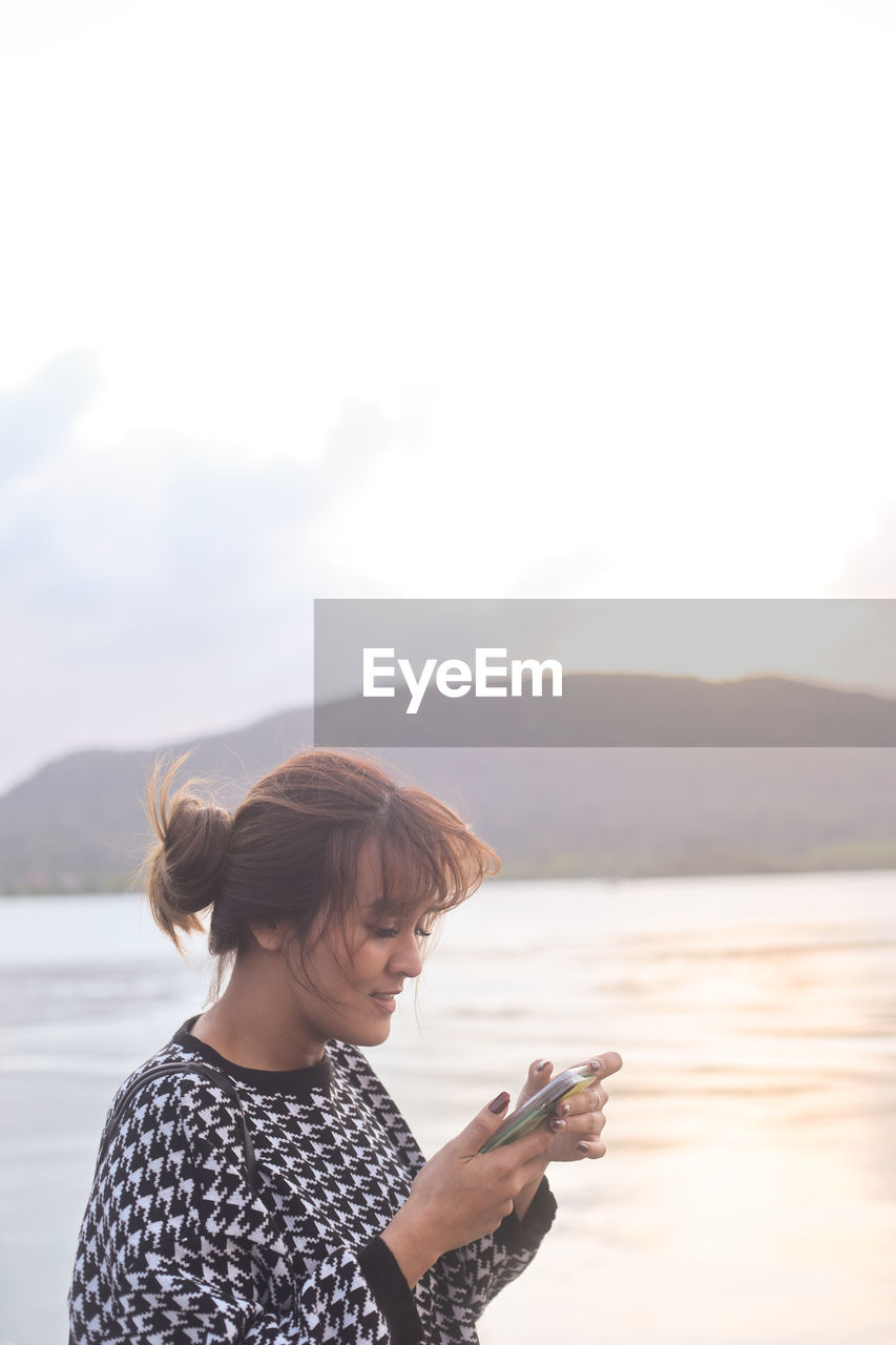 Woman using mobile phone against sea