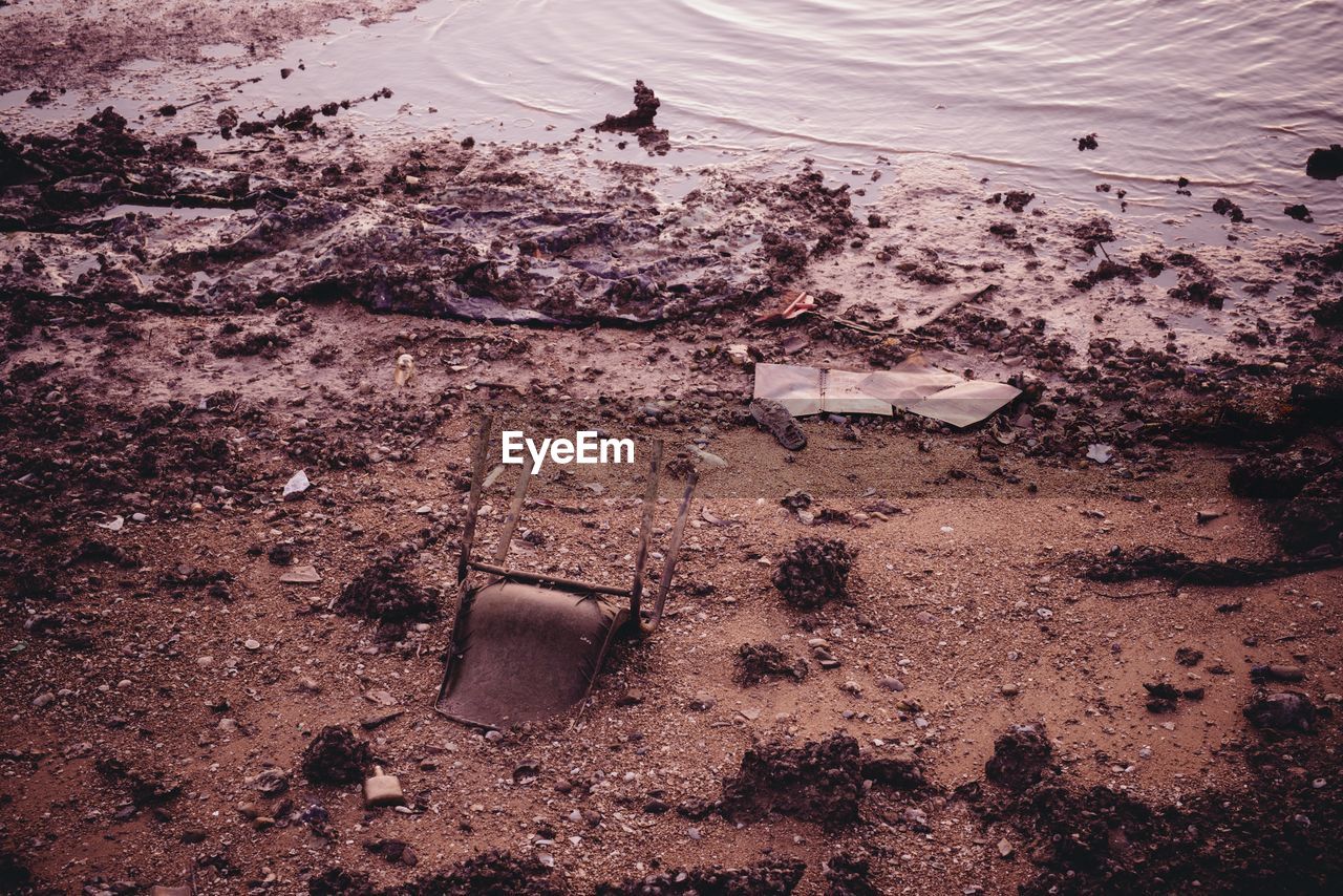 Upside down abandoned chair in sand on seashore during sunset