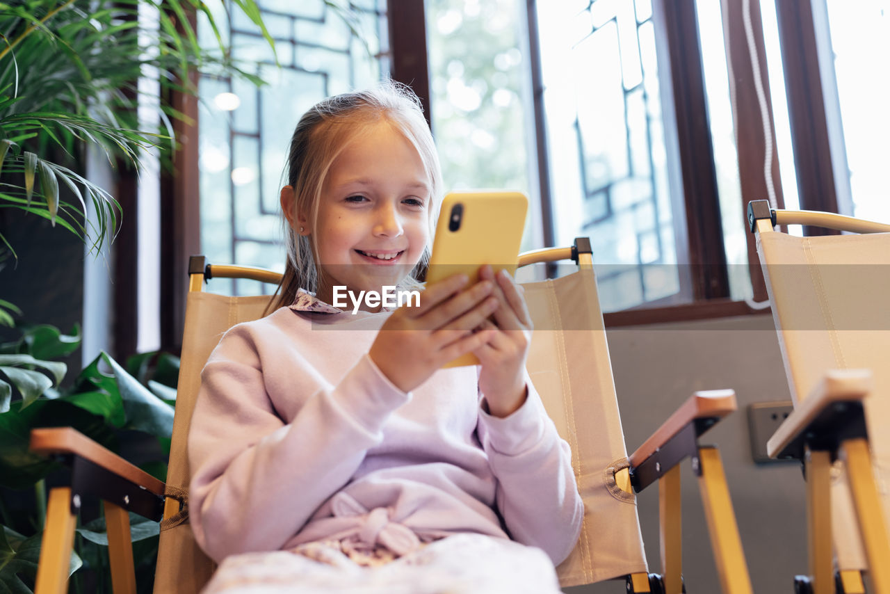 portrait of young woman using mobile phone while sitting on sofa at home