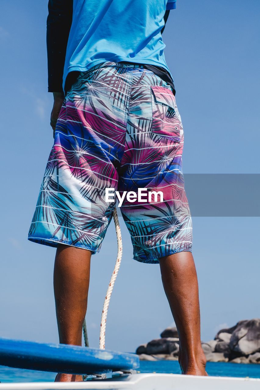 Low section of man standing on boat in sea against clear blue sky