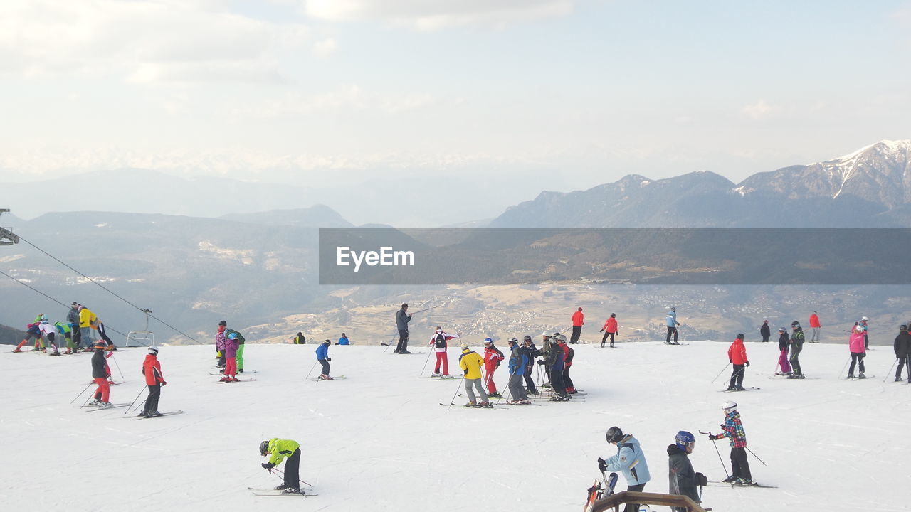 People skiing on mountain against sky during winter