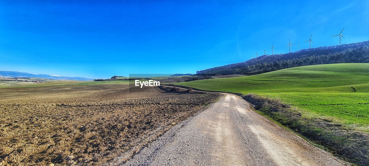 landscape, environment, sky, road, land, scenics - nature, nature, hill, horizon, field, transportation, rural scene, grassland, beauty in nature, blue, plain, rural area, plant, travel, no people, tranquility, agriculture, dirt road, grass, prairie, tranquil scene, plateau, non-urban scene, the way forward, environmental conservation, dirt, cloud, outdoors, travel destinations, day, green, sunlight, farm, clear sky, social issues, country road, sunny, soil, tourism, idyllic, remote, diminishing perspective, summer