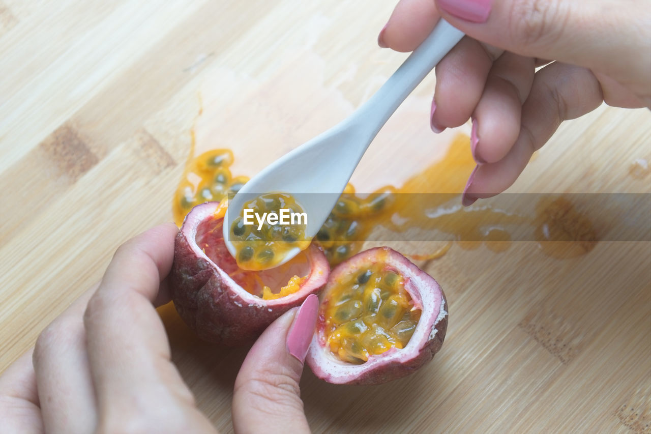 High angle view of woman hands holding passion fruit and spoon on table