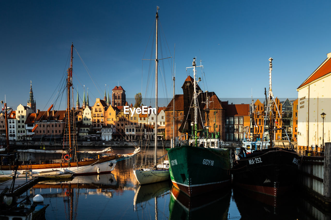 SAILBOATS MOORED IN HARBOR BY BUILDINGS IN CITY