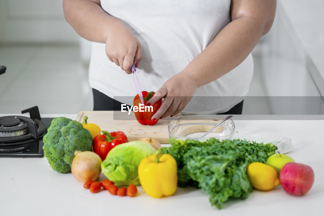 Midsection of woman cutting red bell pepper on cutting board in kitchen