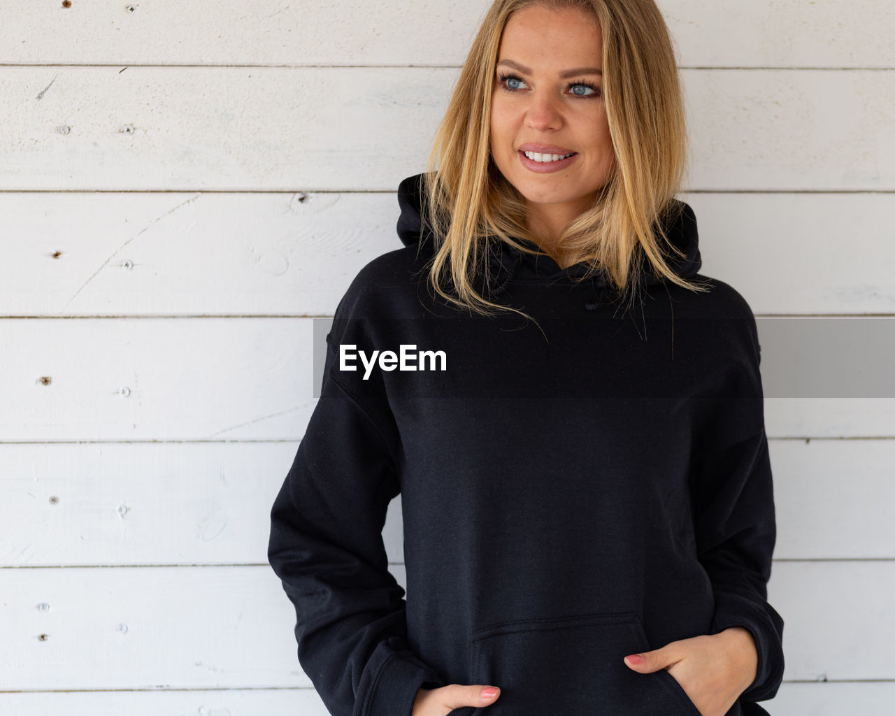 A smiling woman in a black sweatshirt on a background of white boards,. mockup for clothes.