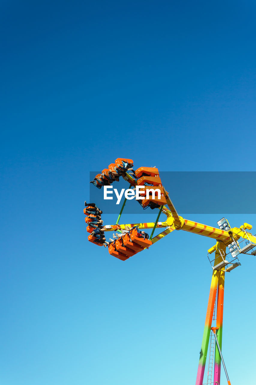 Low angle view of amusement park ride against clear blue sky