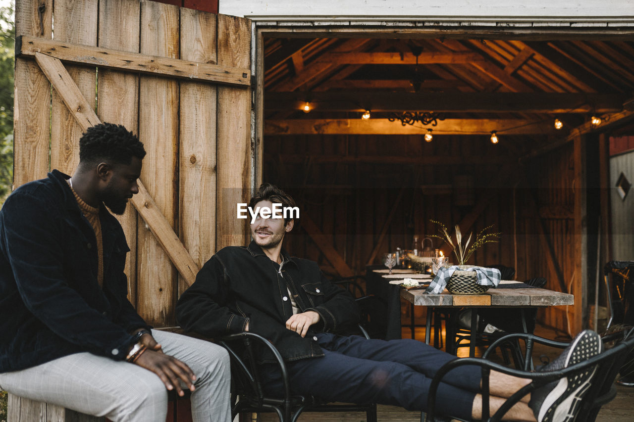 Smiling male friends talking outside cottage during social gathering