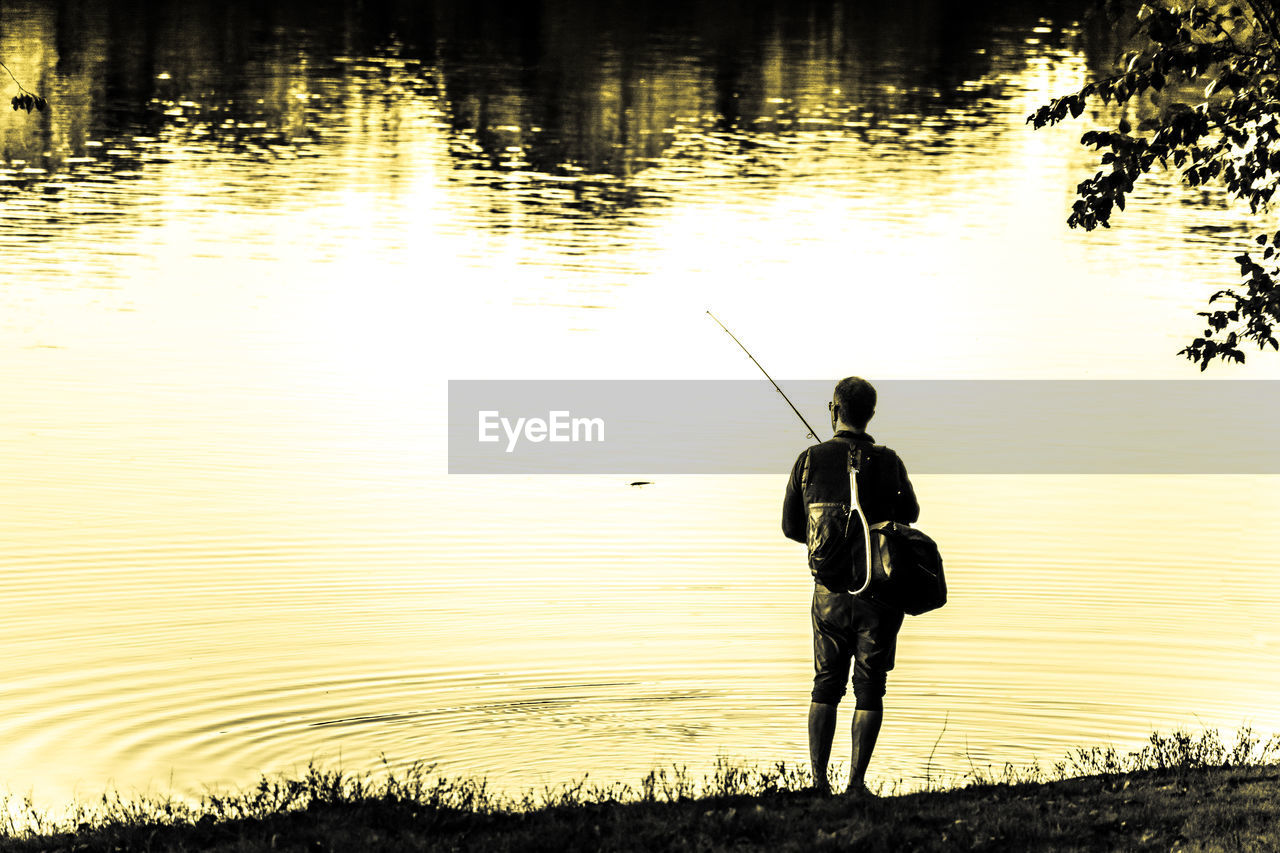 REAR VIEW OF MAN FISHING ON LAKE