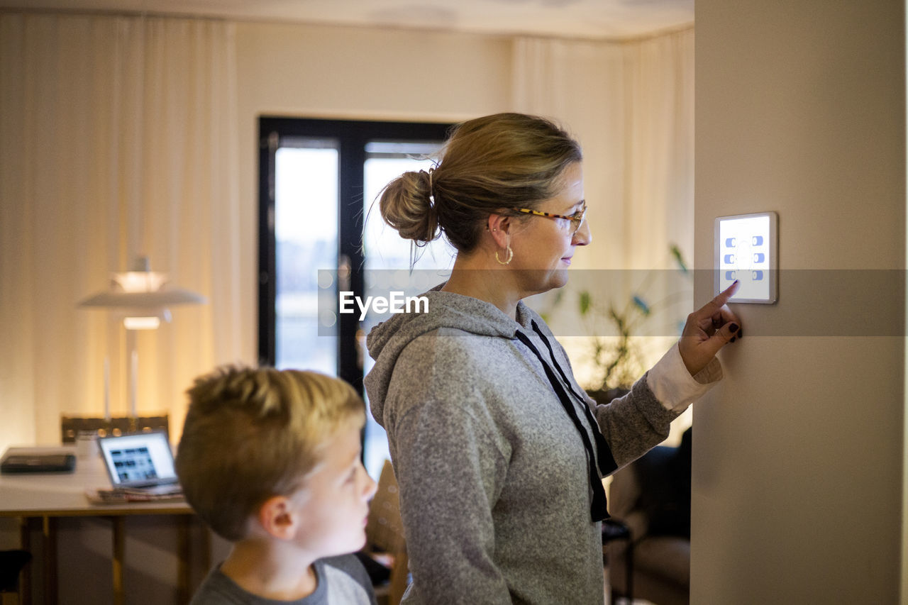 Son looking at mother using digital tablet mounted on wall at smart home