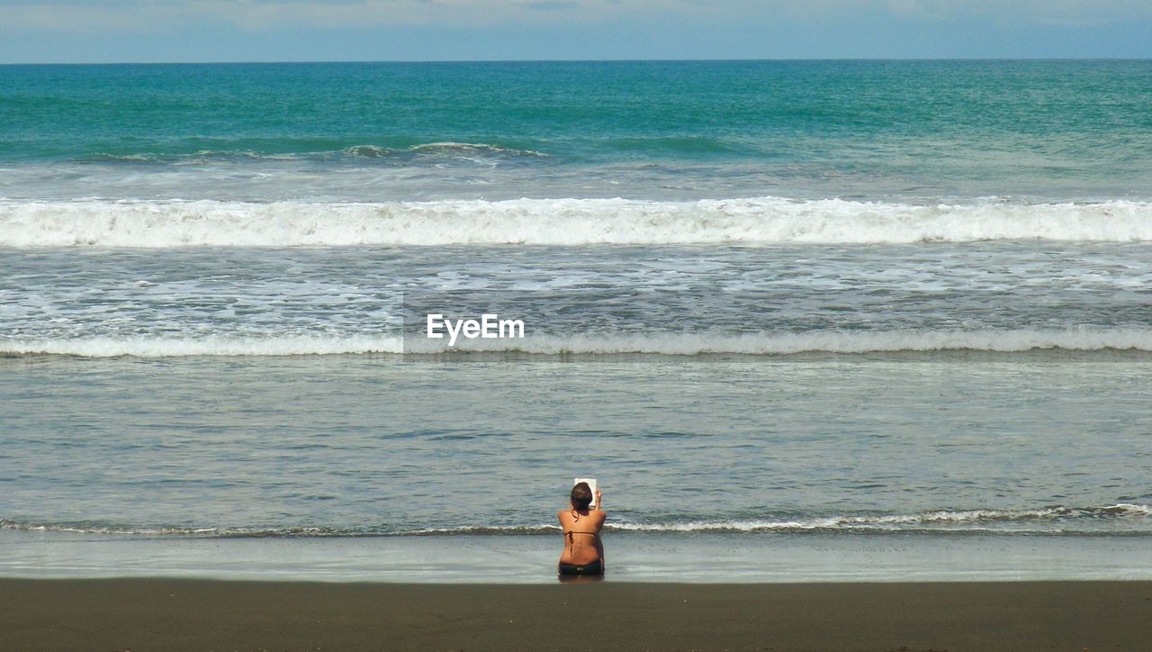 Rear view of woman sitting at beach during sunny day