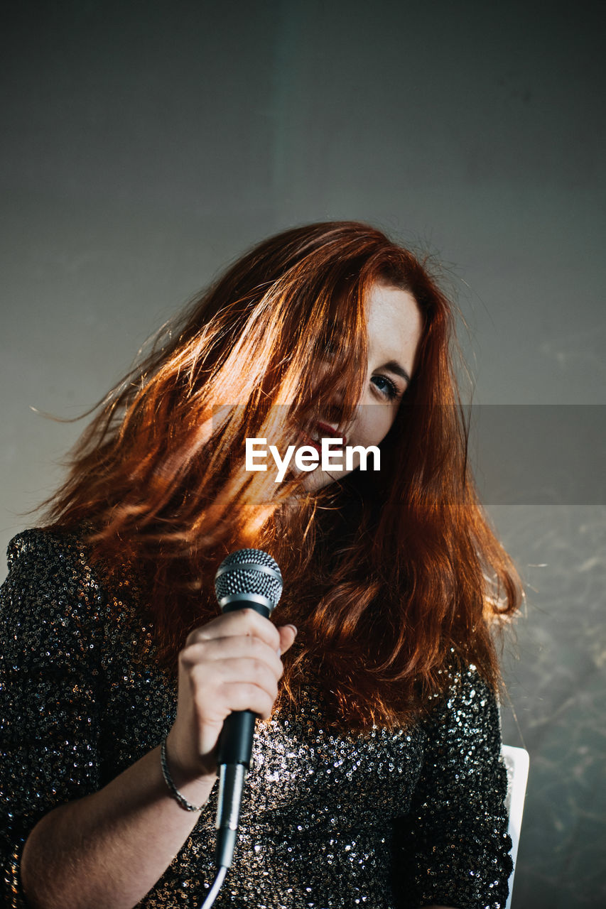 Portrait of redhead female singer woman in sparkly evening dress holding microphone. singer at