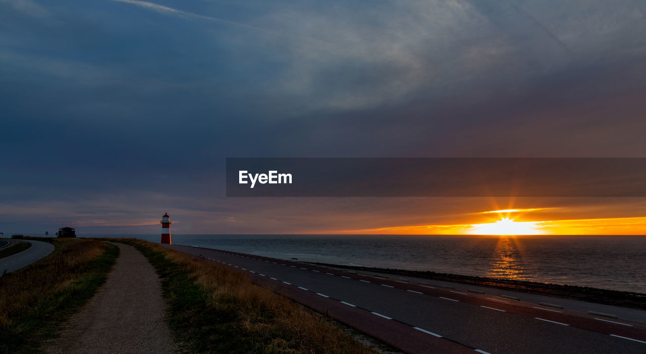 Scenic view of road by sea against sky during sunset