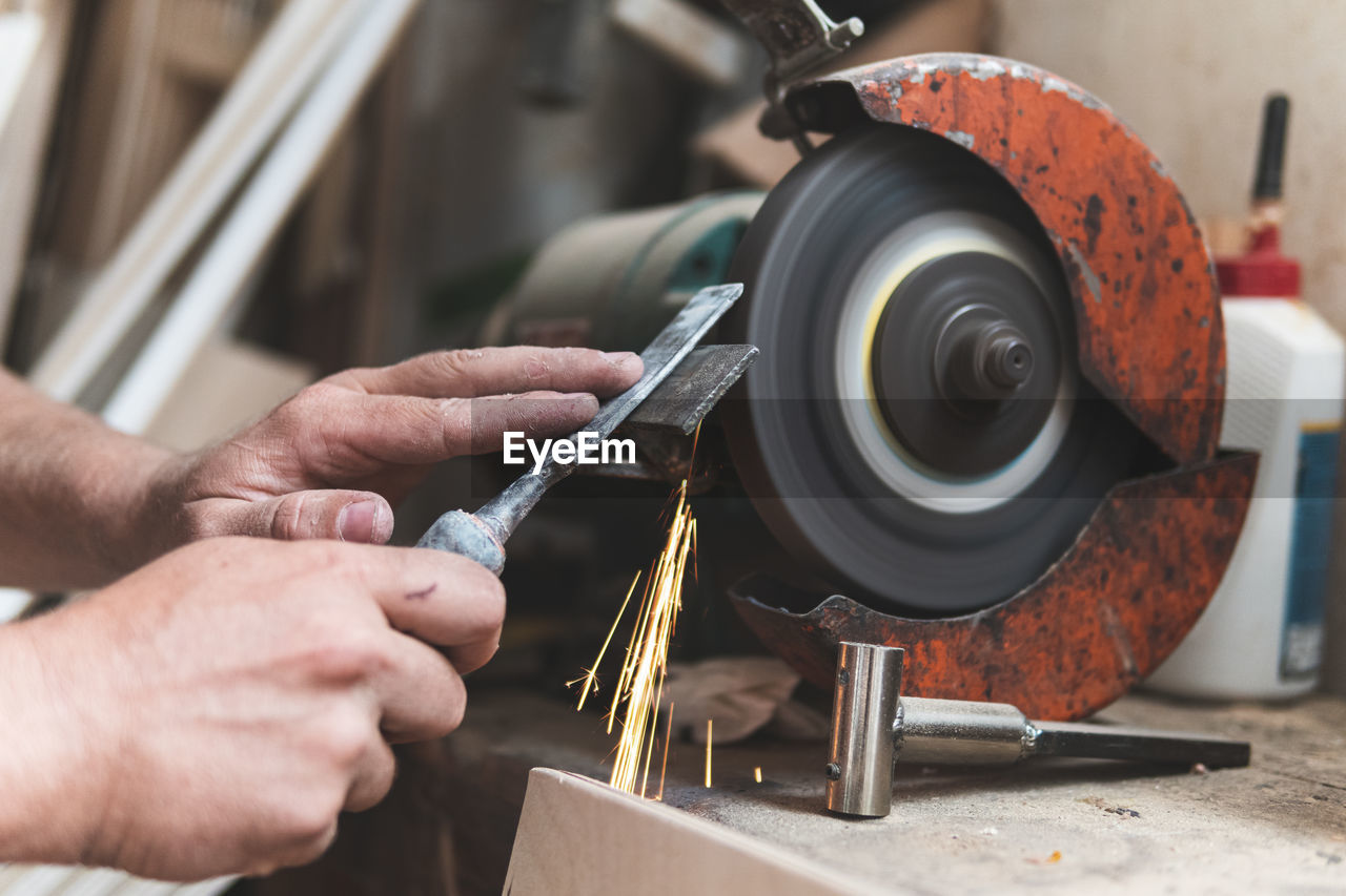 Male carpenter sharpening chisel using grinder in workshop