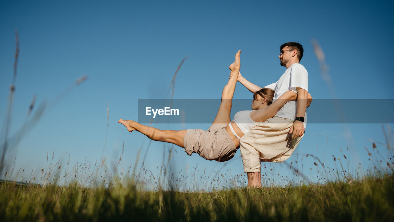 Man and woman dressed alike doing difficult pose while practicing yoga outdoors in the field