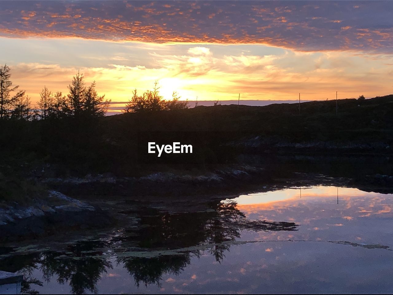 SCENIC VIEW OF LAKE BY SILHOUETTE TREES AGAINST ORANGE SKY