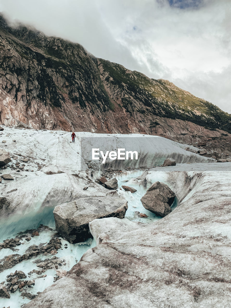 Female hiker on glacier crossing a melt water river on mer de glace