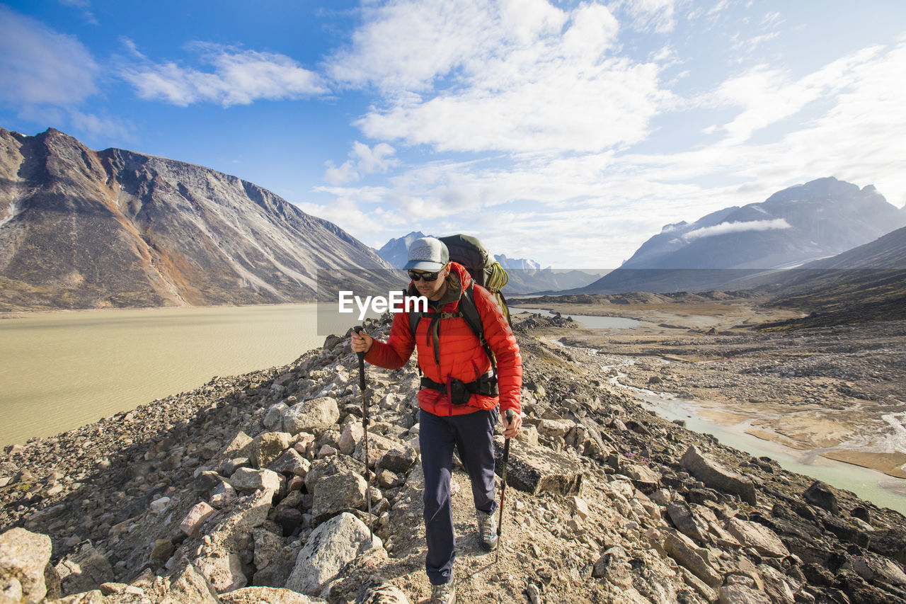 Backpacker wearing warm red jacket hiking over rugged terrain.