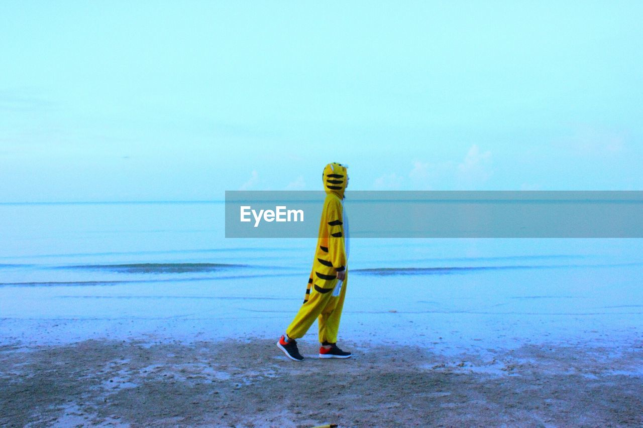 Side view of person in tiger costume walking at beach