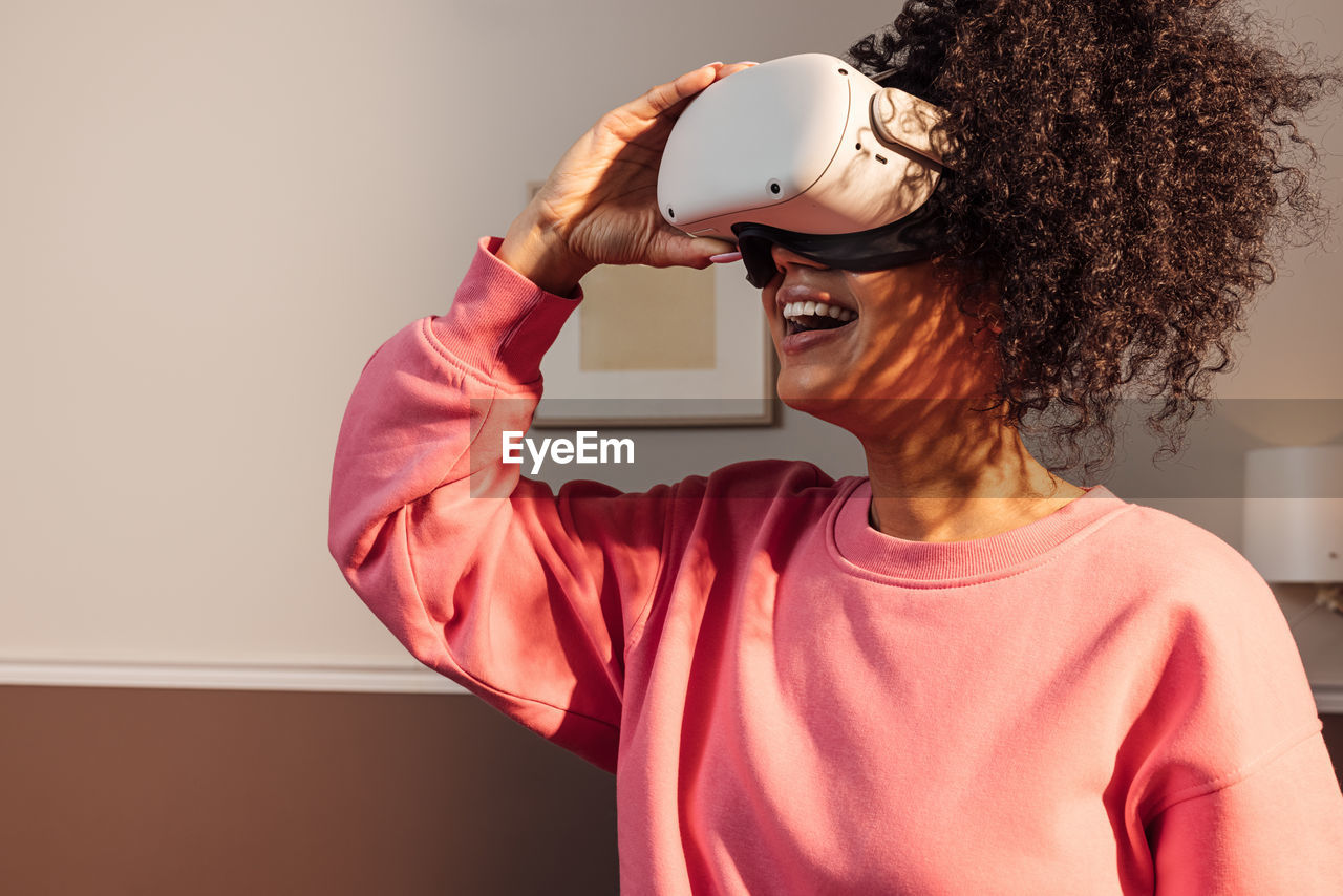 Cheerful woman in casuals standing indoors exploring virtual reality	