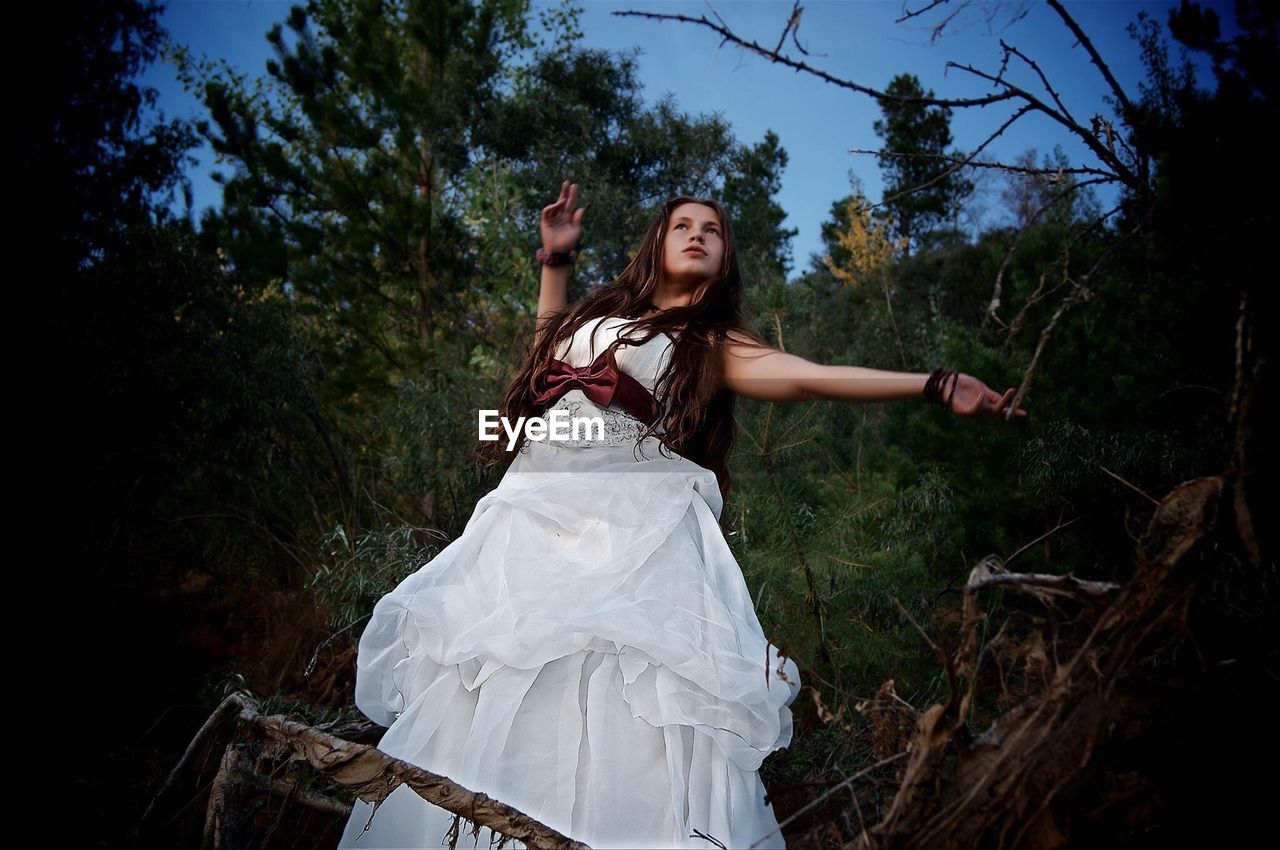 Low angle view of young woman wearing white dress while standing in forest