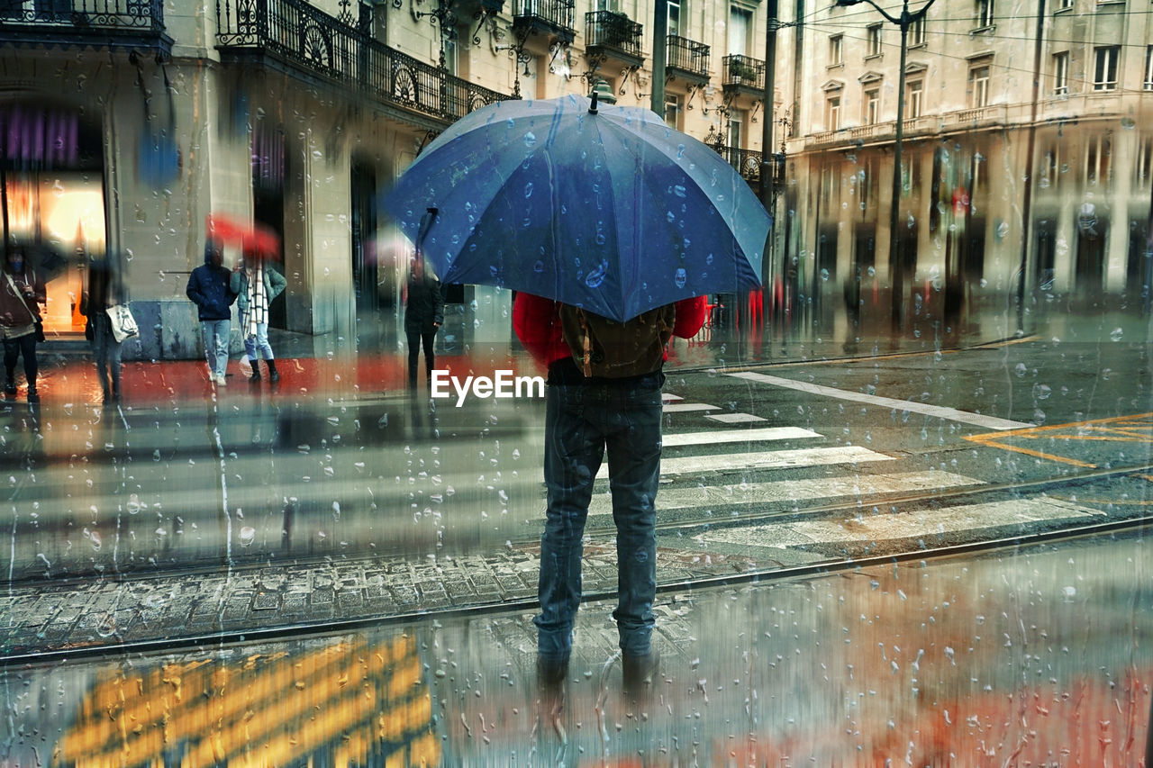 umbrella, rain, wet, protection, rainy season, monsoon, security, water, city, architecture, drop, winter, street, building exterior, nature, built structure, raindrop, walking, adult, snow, city life, torrential rain, storm, fashion accessory, transportation, men, day, outdoors, road, women, one person, reflection, city street, crossing, urban area, extreme weather, parasol, sheltering, motion, lifestyles, standing, full length