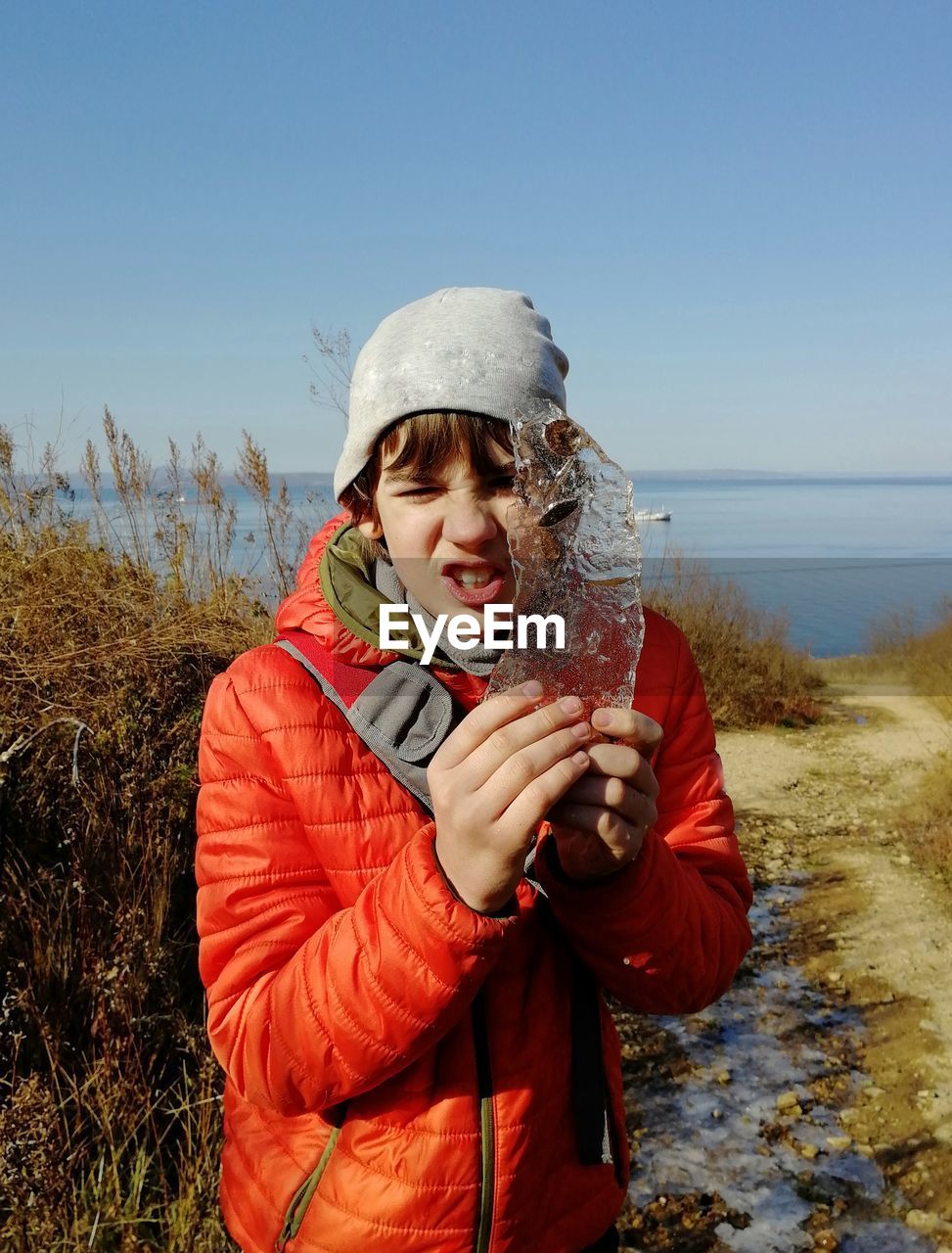 Portrait of teenager boy with piece of ice against sky