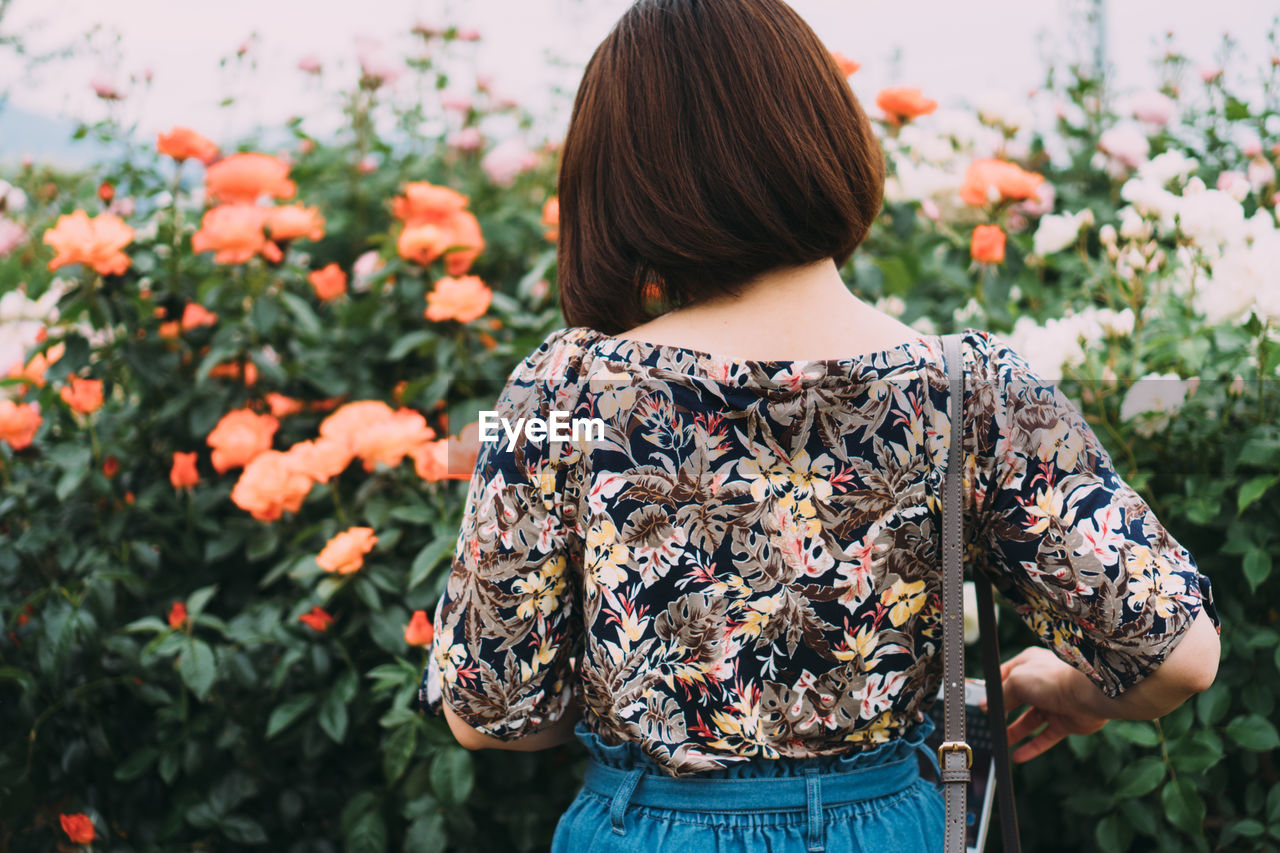 REAR VIEW OF WOMAN STANDING BY FLOWERING PLANT