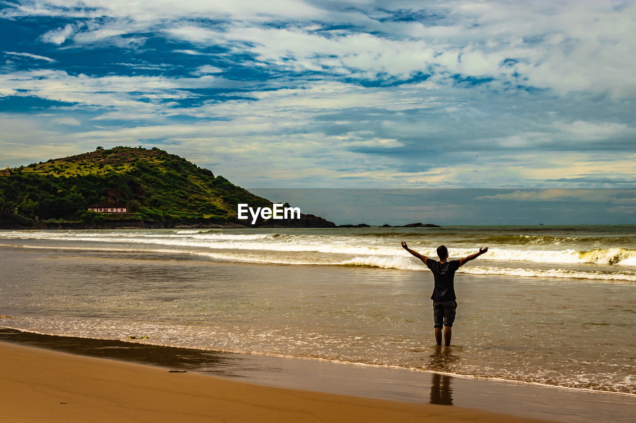 MAN STANDING ON BEACH AGAINST SEA