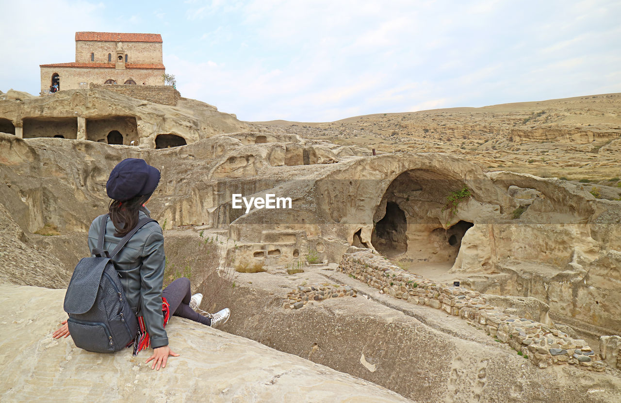 Female visitor sitting on the rock of uplistsikhe cave city ruins, located near gori town in georgia