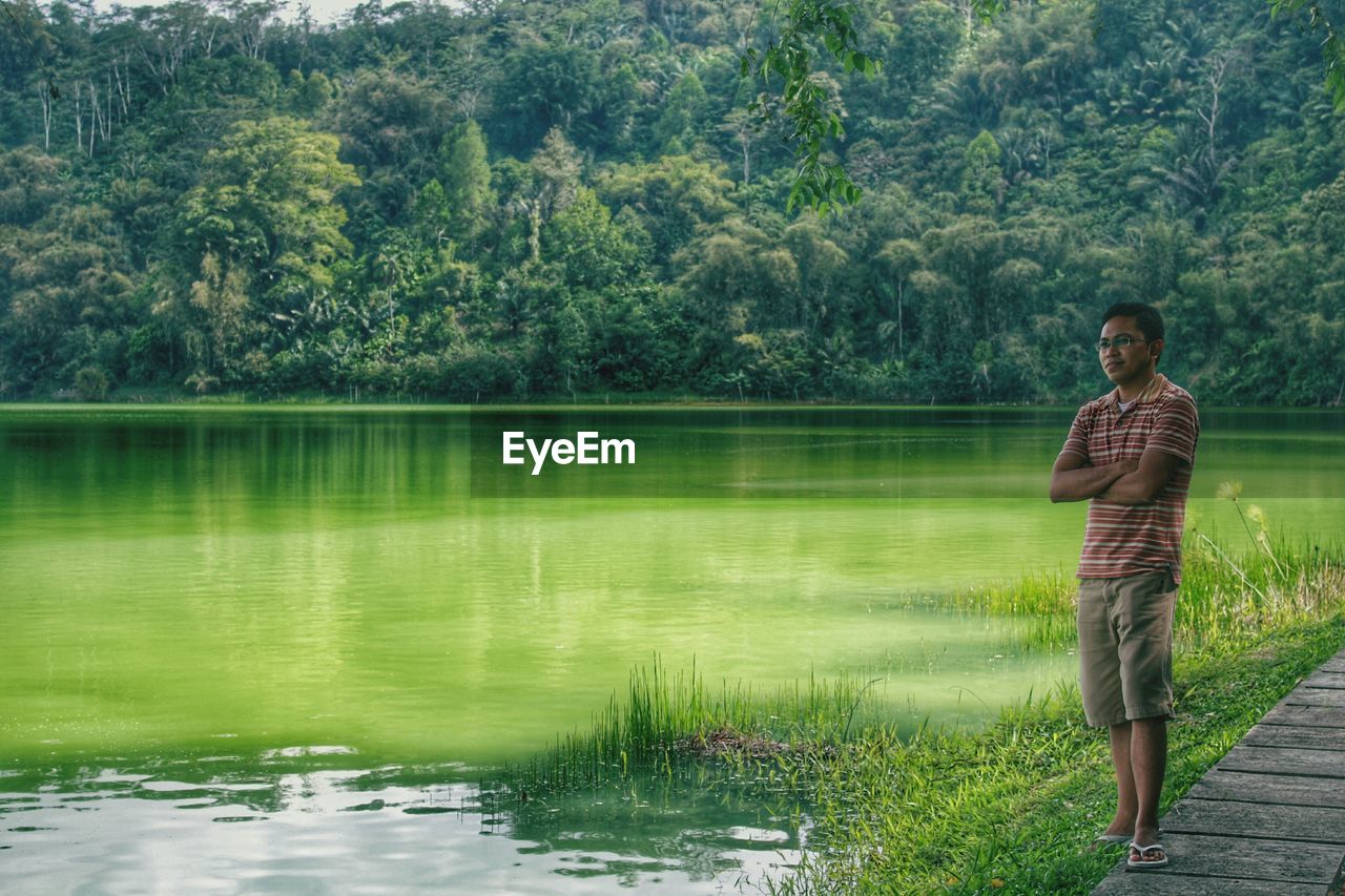 Full length of man with arms crossed standing by lake