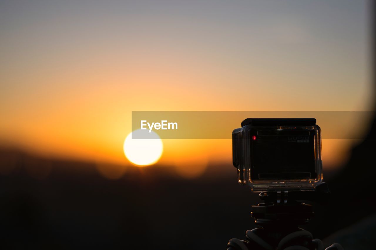 CLOSE-UP OF CAMERA AGAINST ORANGE SKY