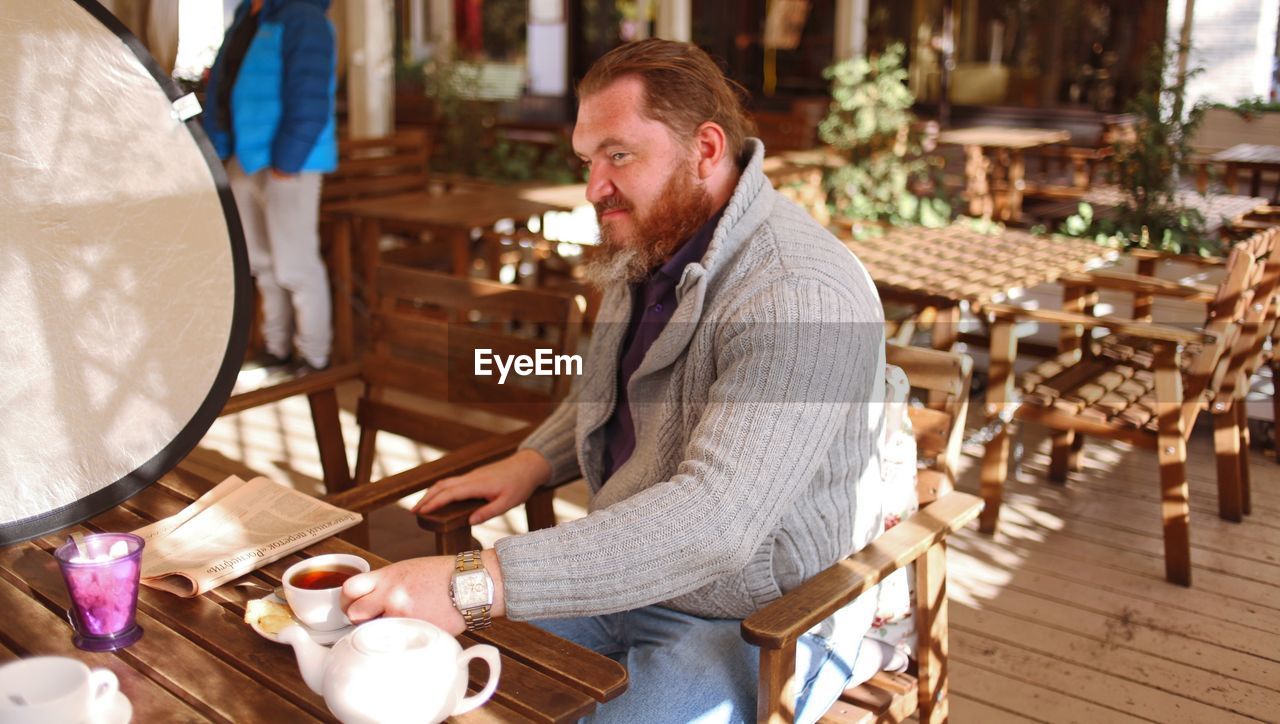 SIDE VIEW OF A MAN SITTING ON TABLE AT CAFE