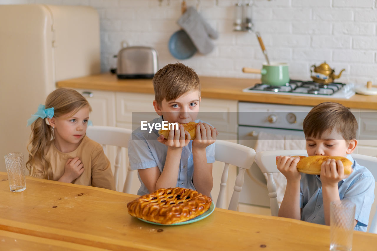 Cheerful children are sitting at table in kitchen, playing with loaf bread