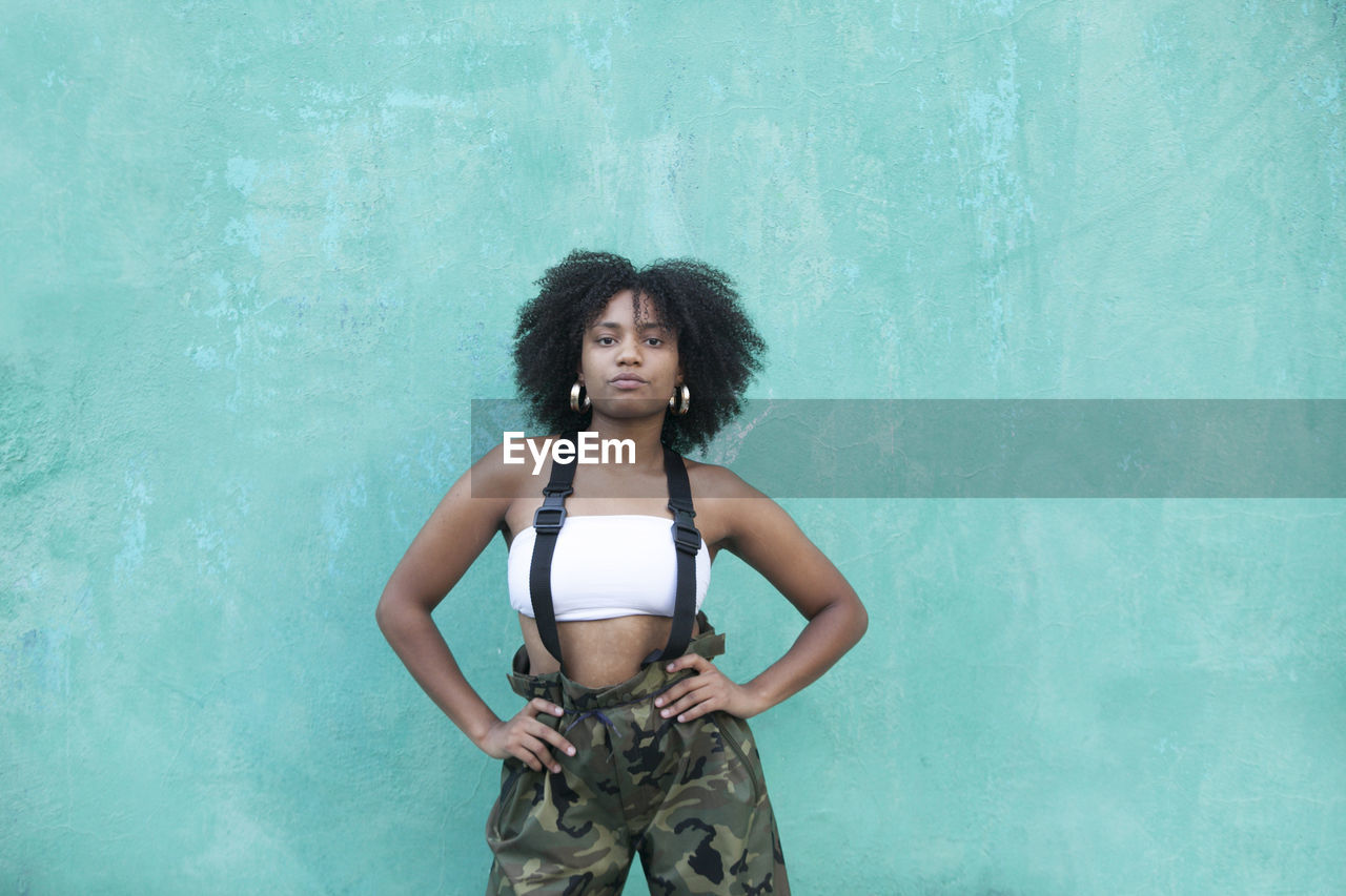 Portrait of young woman with curly hair standing against wall