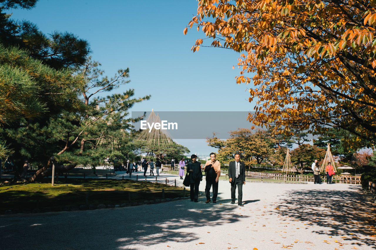 PEOPLE WALKING IN PARK AGAINST CLEAR SKY